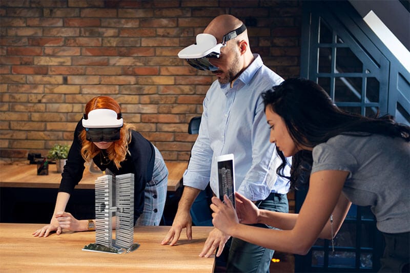 Drei Benutzer:innen betrachten ein Gebäude in Augmented Reality. Dazu verwenden sie verschiedene AR Geräte.